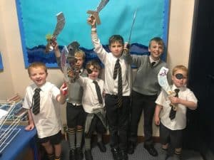 Group of children dressed in school uniforms, holding foam swords and shields, engaging in imaginative play.