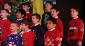 Children singing Christmas carols at Inchmarlo with festive sweaters and joyful expressions.