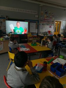Children watching educational video in classroom, engaged and learning actively.