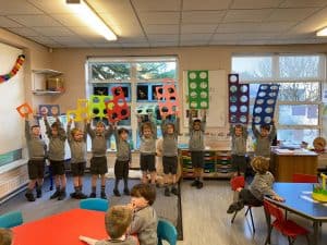 Bright classroom with children holding colorful art displays.