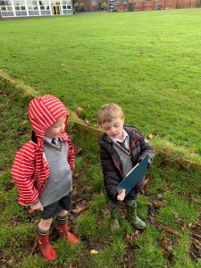 Two children in school uniforms and raincoats playing outdoors on lush green grass at Inchmarlo.