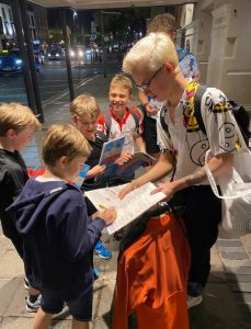 Young children excitedly receiving signed books from an adult outdoors.