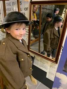 Child in World War II uniform looking at a mirror exhibit.