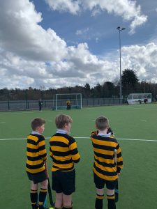 Young boys in black and yellow striped jerseys watching a soccer match on a turf field.