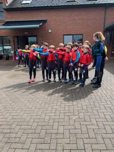 Children in red and blue uniforms with teacher outside school building.