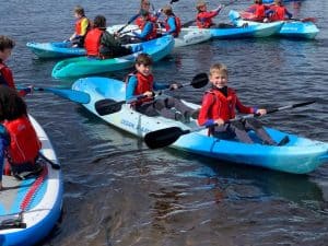 Children kayaking on calm waters at Inchmarlo outdoor activity center.