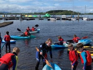 Kids kayaking and paddleboarding at Inchmarlo outdoor activity center. Family-friendly water sports in a scenic setting.