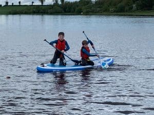 Two children kayaking on a peaceful lake at Inchmarlo, enjoying outdoor water activities in a scenic setting.