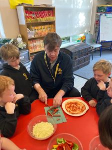 Young teacher demonstrating pizza preparation to students.