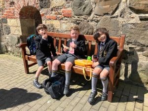 Three children in school uniforms sitting on a wooden bench outside Inchmarlo, enjoying a break.