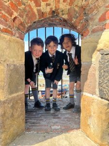 Three children smiling at Inchmarlo school archway, enjoying outdoor activity, highlighting school spirit.