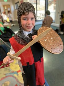 Young girl in knight costume holding shield and sword at Inchmarlo indoor event.