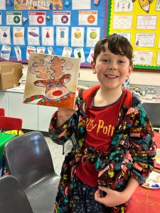 Child holding Christmas craft artwork in classroom.