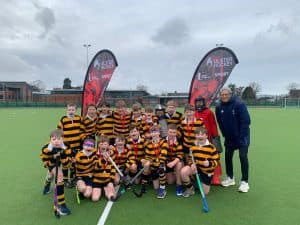 Youth hockey team posing with sticks and gear on a field with banners in the background.