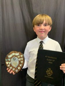 Young boy in school uniform holding a shield and certificate celebrating academic achievement.