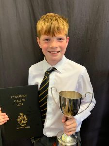 Young boy in school uniform holding trophy and certificate, celebrating achievement at Inchmarlo.