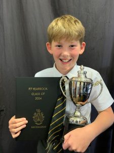 Happy boy holding a trophy and certificate at Inchmarlo School, celebrating academic achievement.