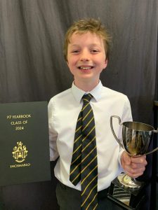 Young boy holding a trophy celebrating academic success, standing next to certificate.