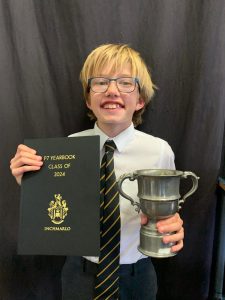 Happy boy holding award and trophy at Inchmarlo School graduation.