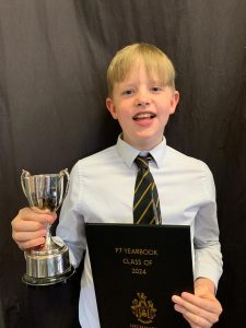 Young boy celebrating academic success with trophy and diploma at Inchmarlo School.