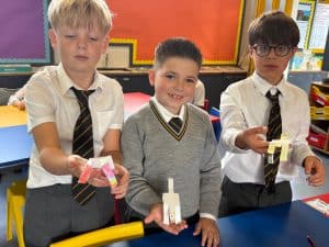 Three schoolboys in uniforms showing student projects in a classroom setting.