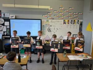 Students holding books in classroom with educational posters.