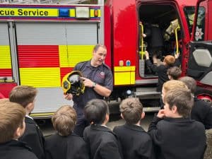 Firefighter showing rescue equipment to students outside fire truck.