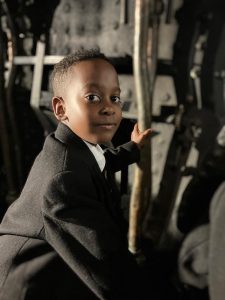 Young boy in formal attire at Inchmarlo estate, surrounded by outdoor furniture.