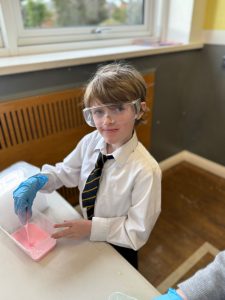 Young student conducting science experiment with safety gloves and goggles at Inchmarlo.