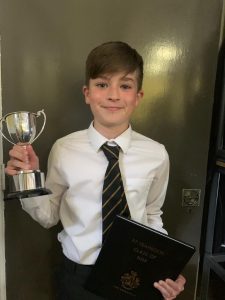 Young boy holding trophy and certificate at Inchmarlo School, celebrating academic success.