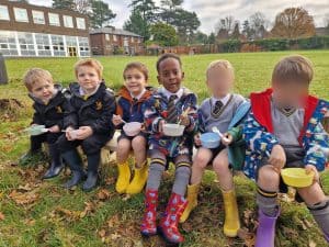 Six children sitting on grass in school uniforms and rain boots at Inchmarlo school.