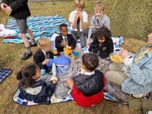 Children sitting around teacher outdoors.
