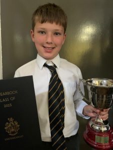 Young boy in school uniform holding a trophy and certificate, celebrating achievement at Inchmarlo.