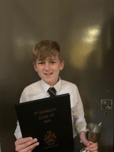 Young boy holding award and glass of water, celebrating achievement at Inchmarlo School.