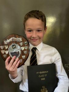 Young boy holding an award and a Yearbook.