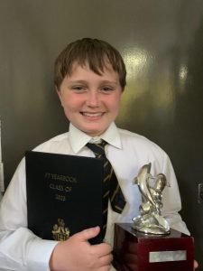 Young student holding a trophy and certificate at Inchmarlo School, showcasing academic achievements and extracurricular success.