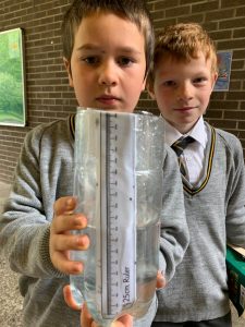 Two children holding a clear water measuring container at Inchmarlo School.
