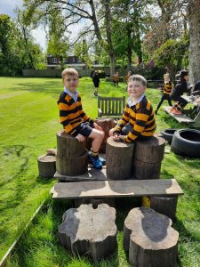 Two boys in school uniforms sitting on wooden stools in Inchmarlo Gardens, enjoying a sunny day at the scenic outdoor space.
