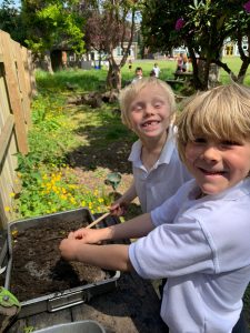 Smiling children planting flowers in Inchmarlo's garden, highlighting outdoor activities and family-friendly environment.