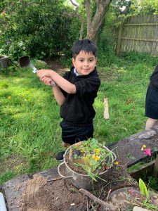 Smiling boy planting flowers in Inchmarlo garden with lush greenery background.