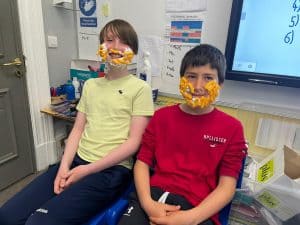 Two children wearing colorful masks in a classroom setting at Inchmarlo.