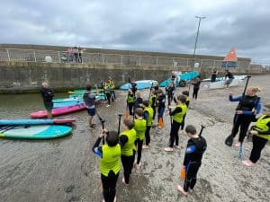 Children learning paddleboarding on the beach with instructors.