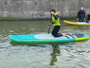 Person kneeling on paddleboard practicing paddle skills on calm water.