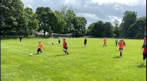 Children playing soccer at Inchmarlo sports field in a lush green park.