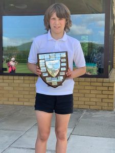 Young student holding school shield with campus background.
