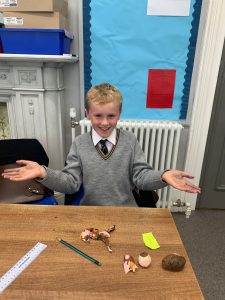 Smiling student presenting clay models at Inchmarlo school classroom.
