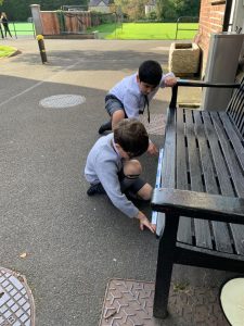 Two children drawing on the ground outside at Inchmarlo, surrounded by greenery and outdoor amenities.