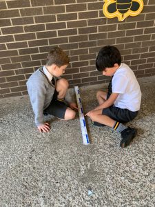 Two children playing with a ruler outside on the ground, enjoying outdoor activities.