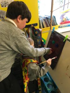 Young children painting at an art station in a colorful classroom.
