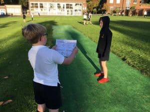 Two children reading outdoors on a sunny day at Inchmarlo, with green grass and trees in the background.